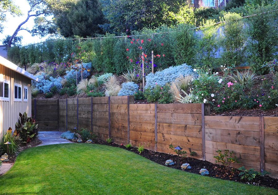 backyard with grass and a wooden retaining wall supporting bushes and flowers