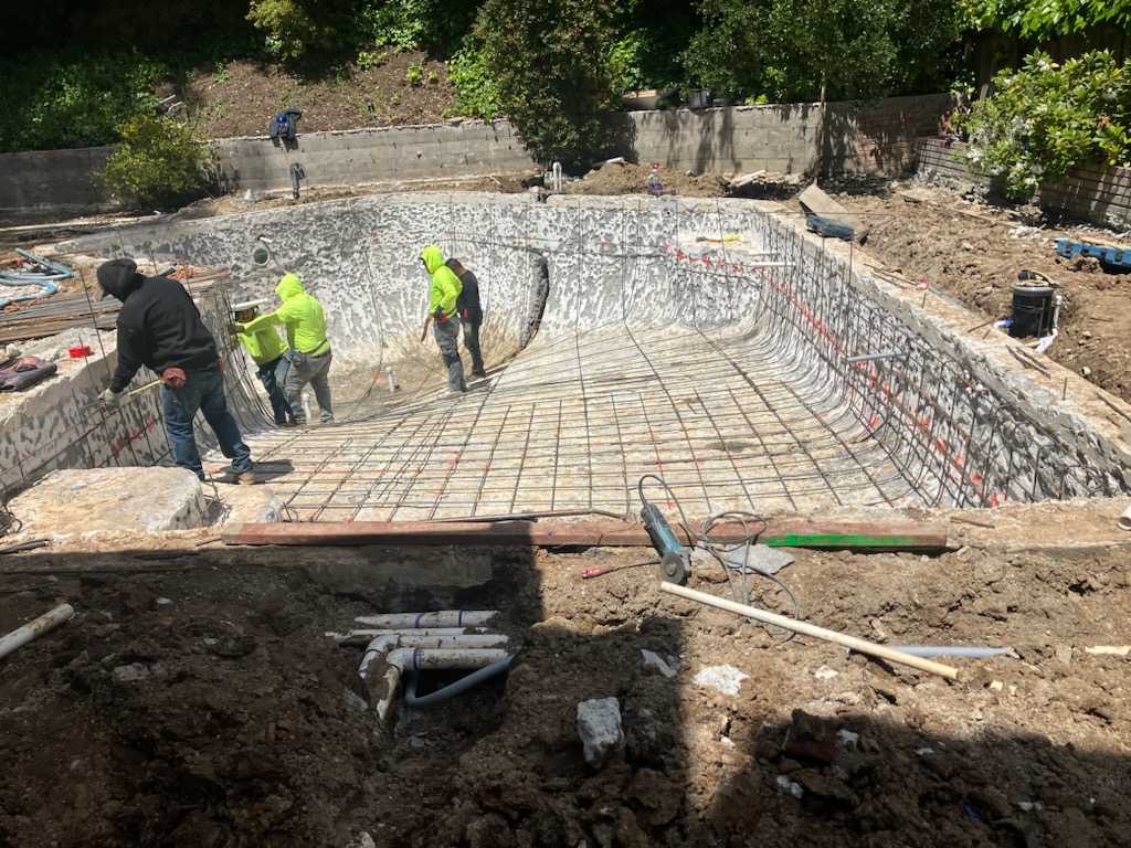 workers stand in an empty ground pool fixing it